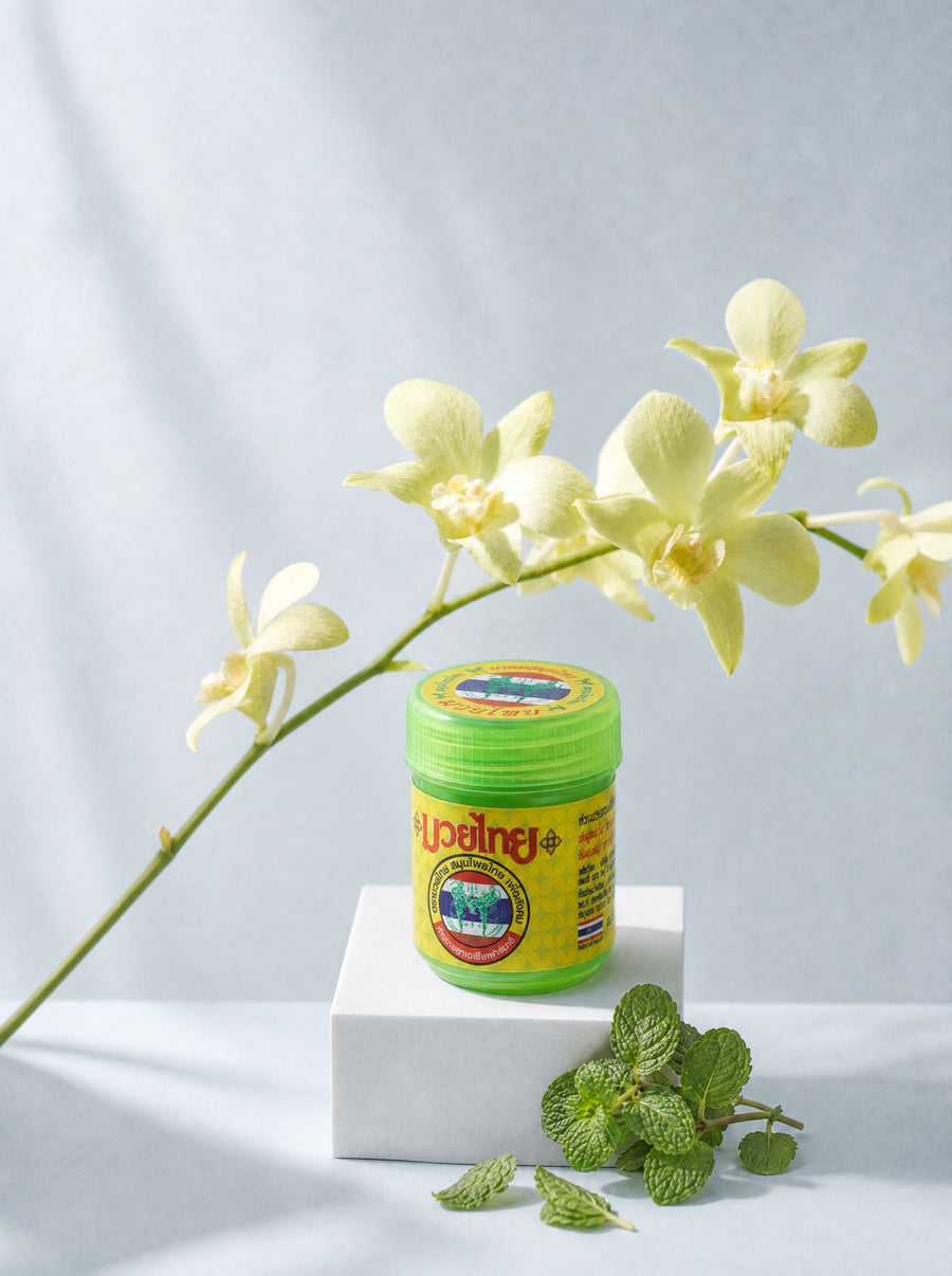 Słoiczek inhalatora Jai Yen na białym podeście, nad nim gałązka orchidei